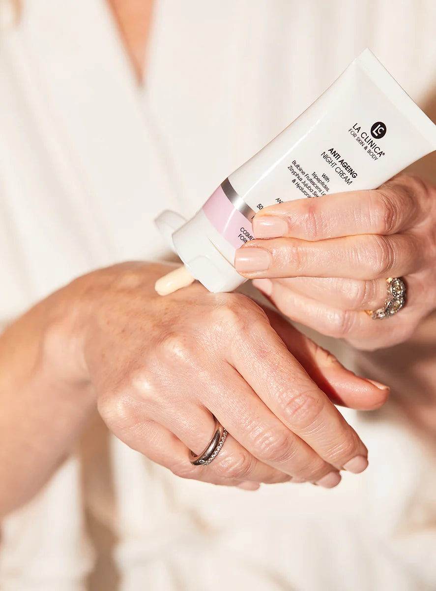 Person applying a Anti Ageing Night Cream With Tripeptides to their hand with a focus on the product and action.