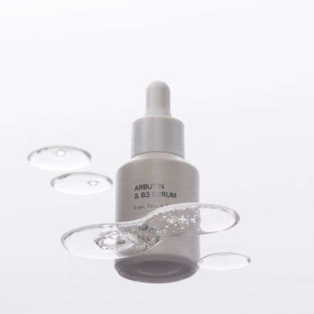 Arbutin & B3 Serum bottle with dropper on a glass background