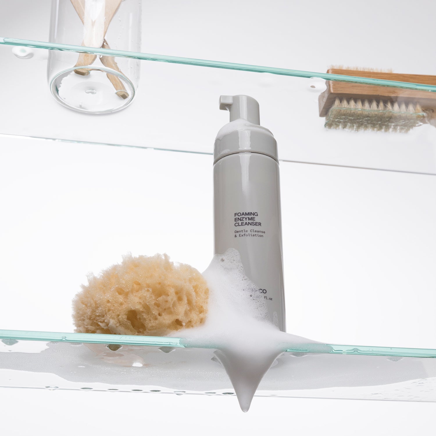 INSKIN.CO Foaming Enzyme Cleanser bottle with a sponge on a glass shelf against a white background