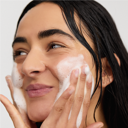Woman applying INSKIN.CO Foaming Enzyme cleanser to her face against a neutral background