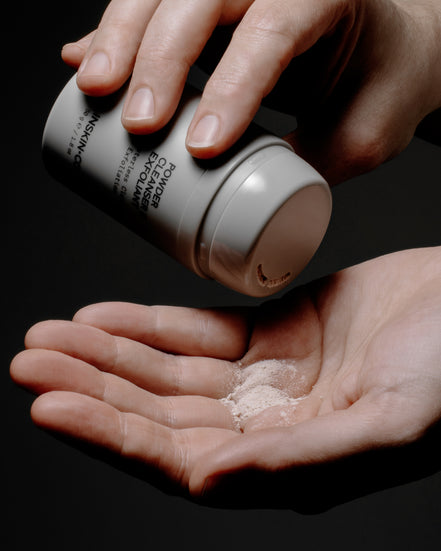 Hand holding  Powder cleanser & Exfoliant and sifting it into an open palm on a black background