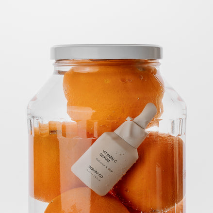 Jar of oranges with a vitamin C serum bottle inside on a white background