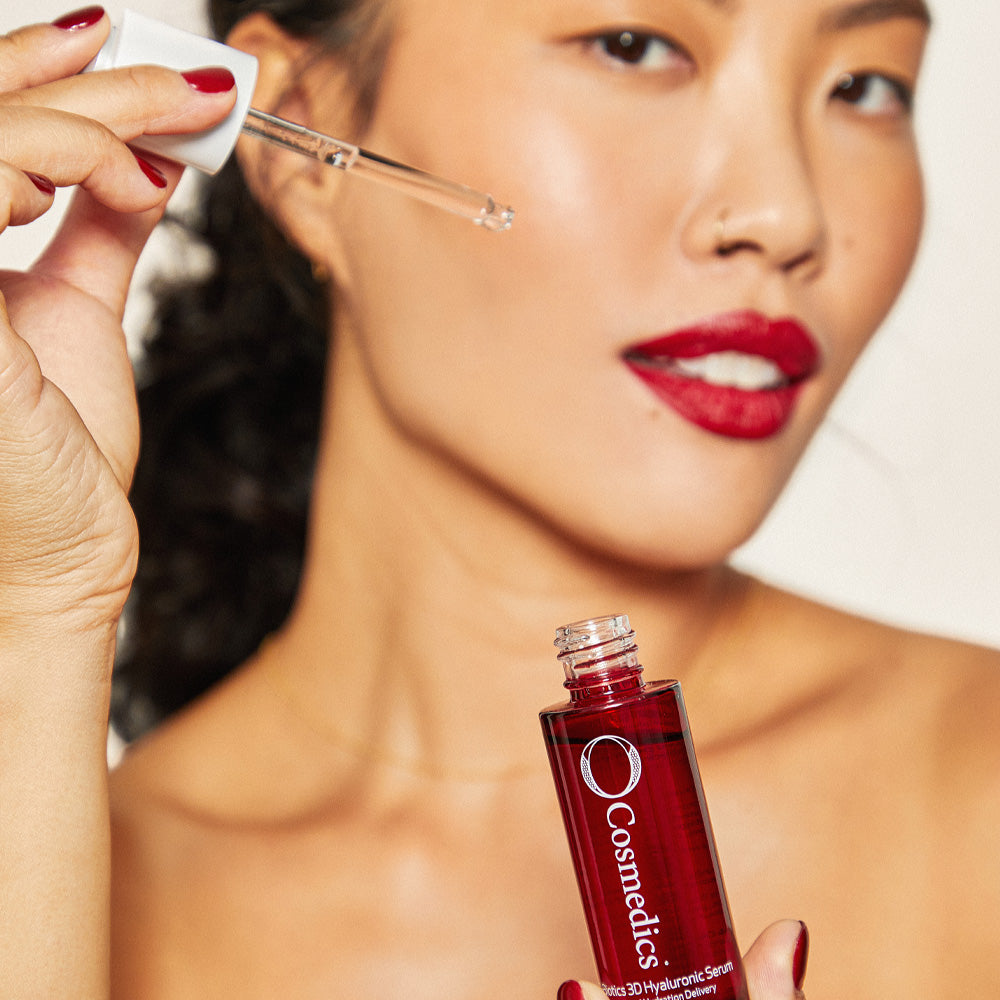 Woman applying 'O' 3D Hyaluronic Serum with a dropper to her face, holding a bottle.