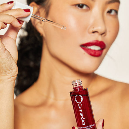 Woman applying 'O' 3D Hyaluronic Serum with a dropper to her face, holding a bottle.