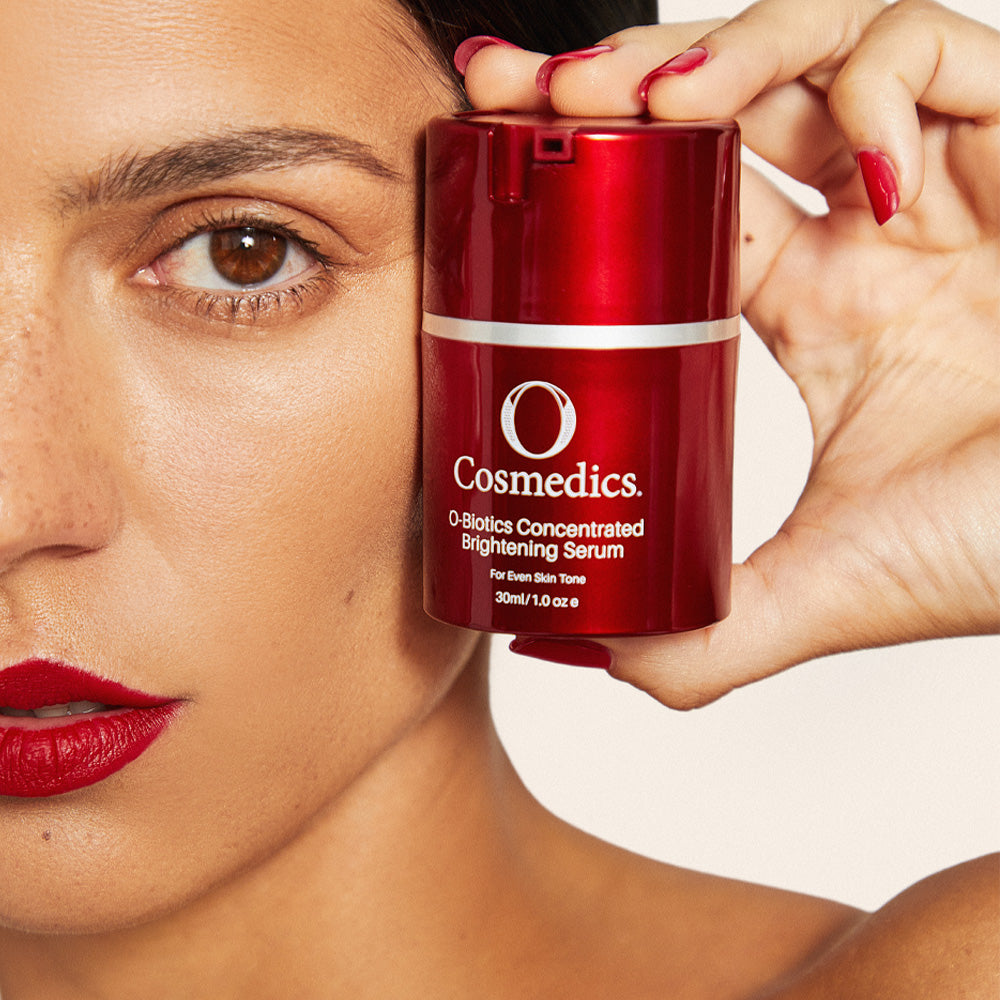 Woman holding a red 'O' Concentrated Brightening Serum can near her face.