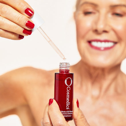 Woman holding 'O' Biotics EGF Booster dropper with a red bottle labeled 'O Cosmetics' against a blurred background.