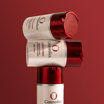 Three bottles of O Cosmedics Comfort Cream stacked on a red background