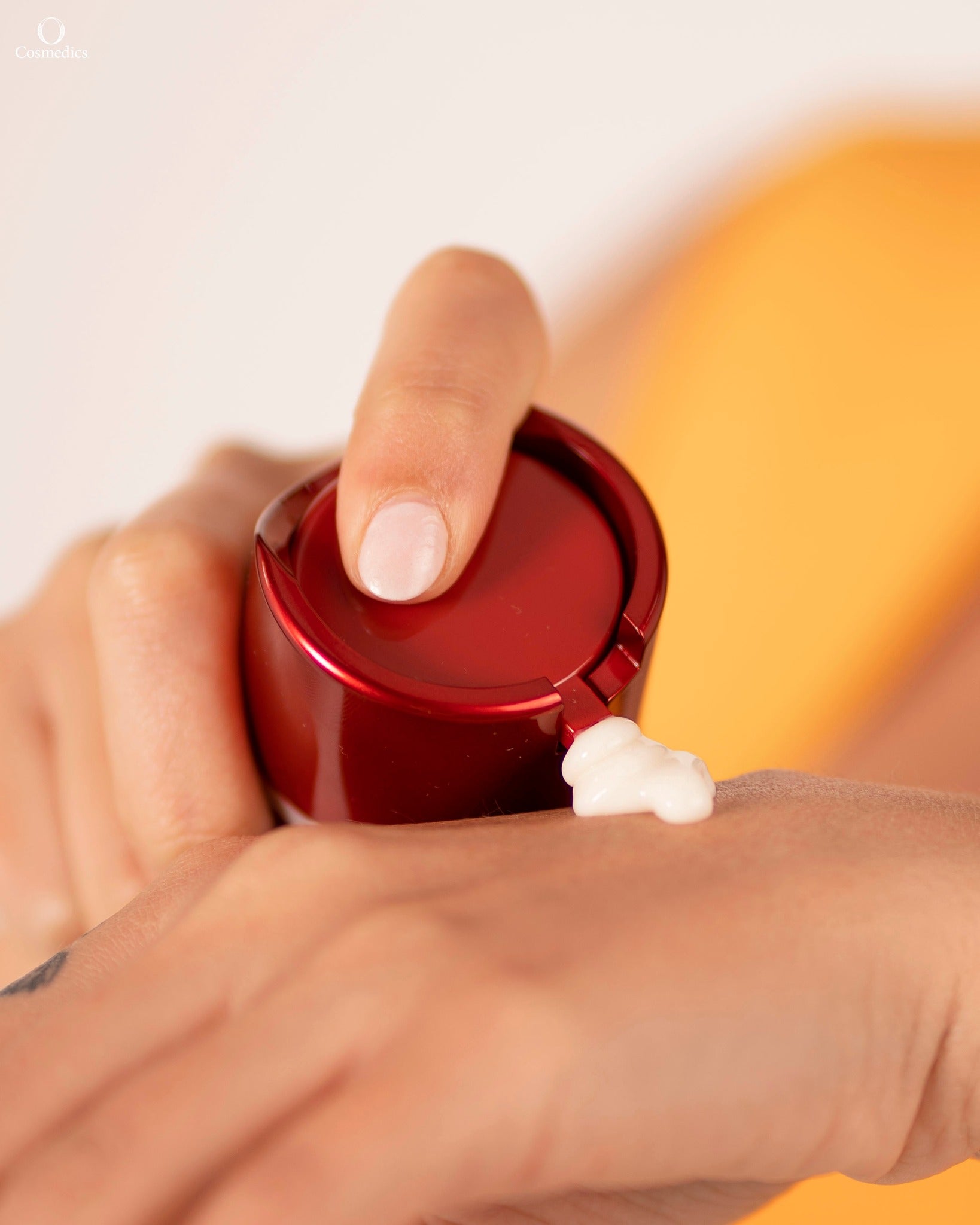 Hand applying 'O' Comfort Cream from a red container on a blurred background