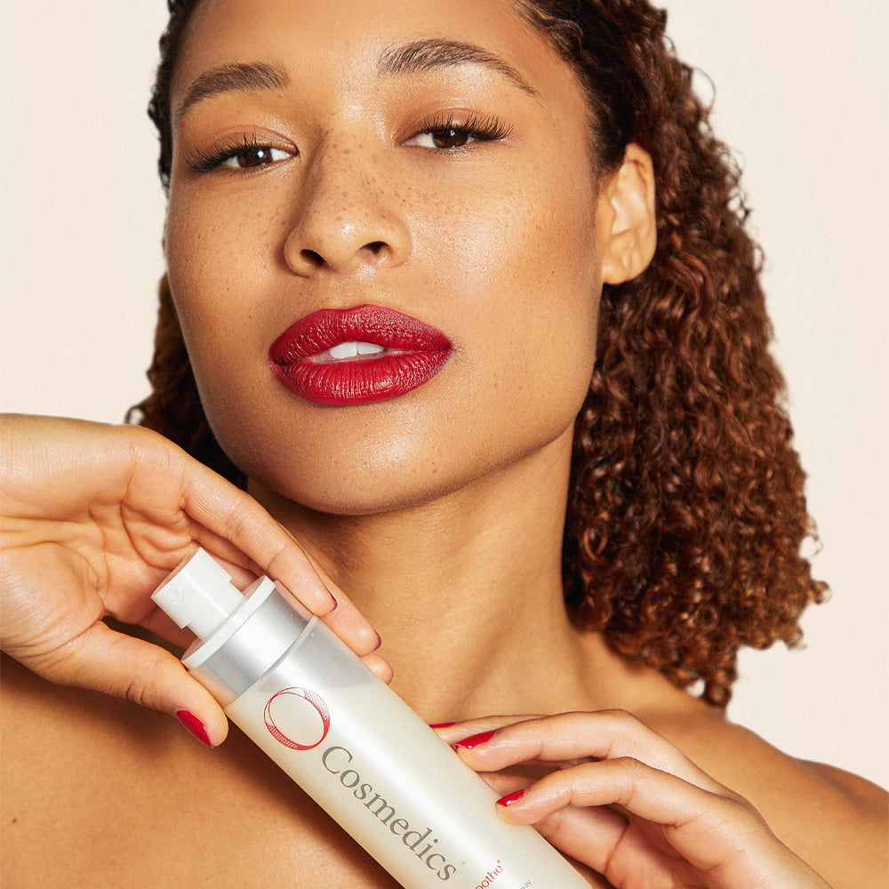 Woman holding O Cosmedics Medi-Soothe Mist Spray against a beige background