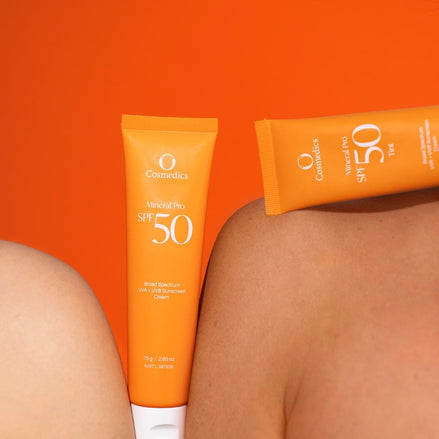 Two tubes of OCosmoetics Sunscreen SPF 50 on a person's shoulder against an orange background