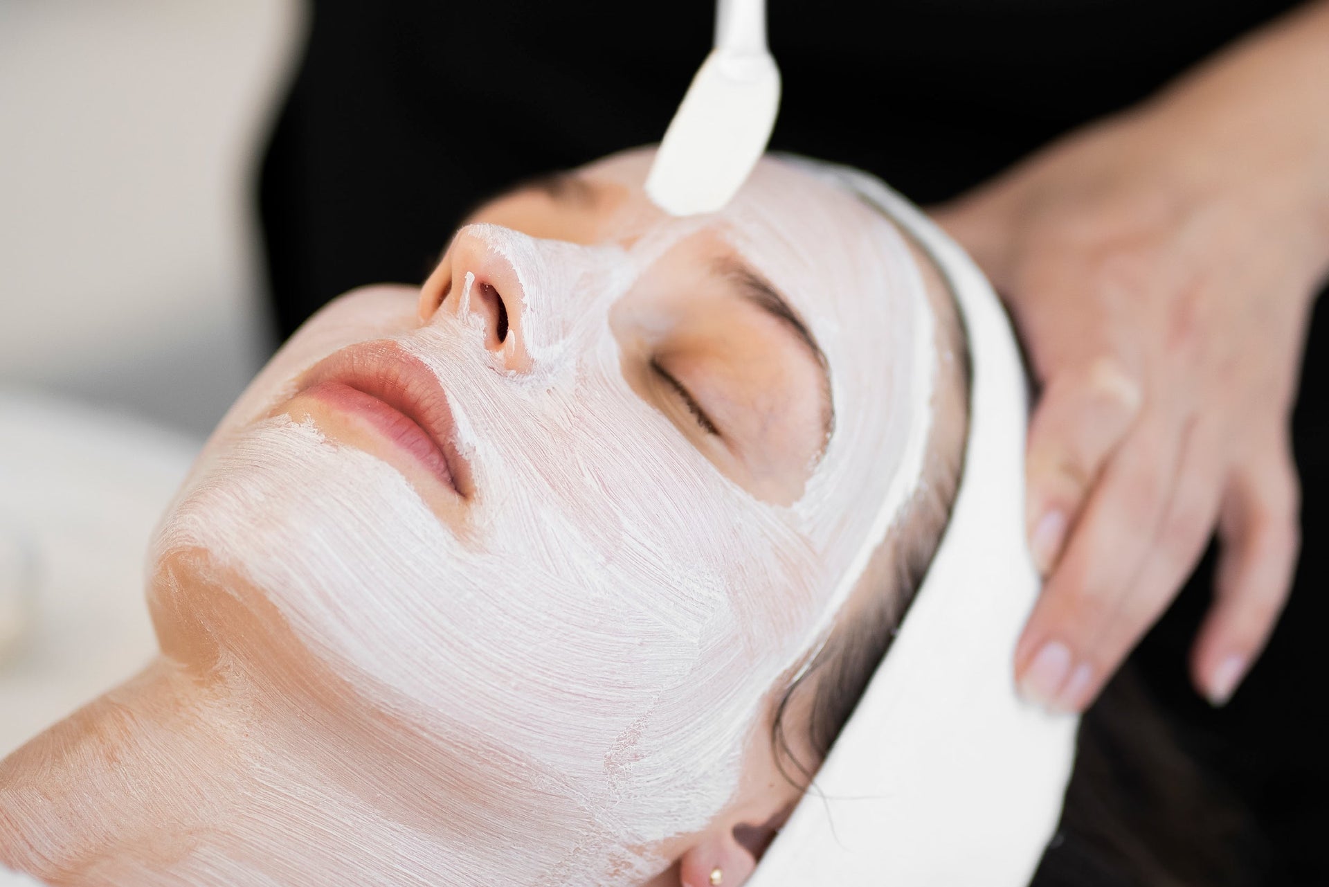 Person receiving a facial treatment with a white mask on their face.