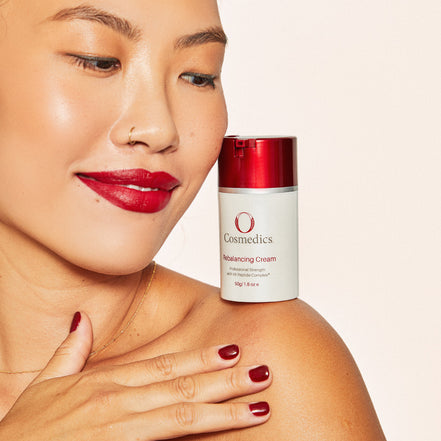 Woman with red lipstick holding 'O' Rebalancing Cream on a beige background