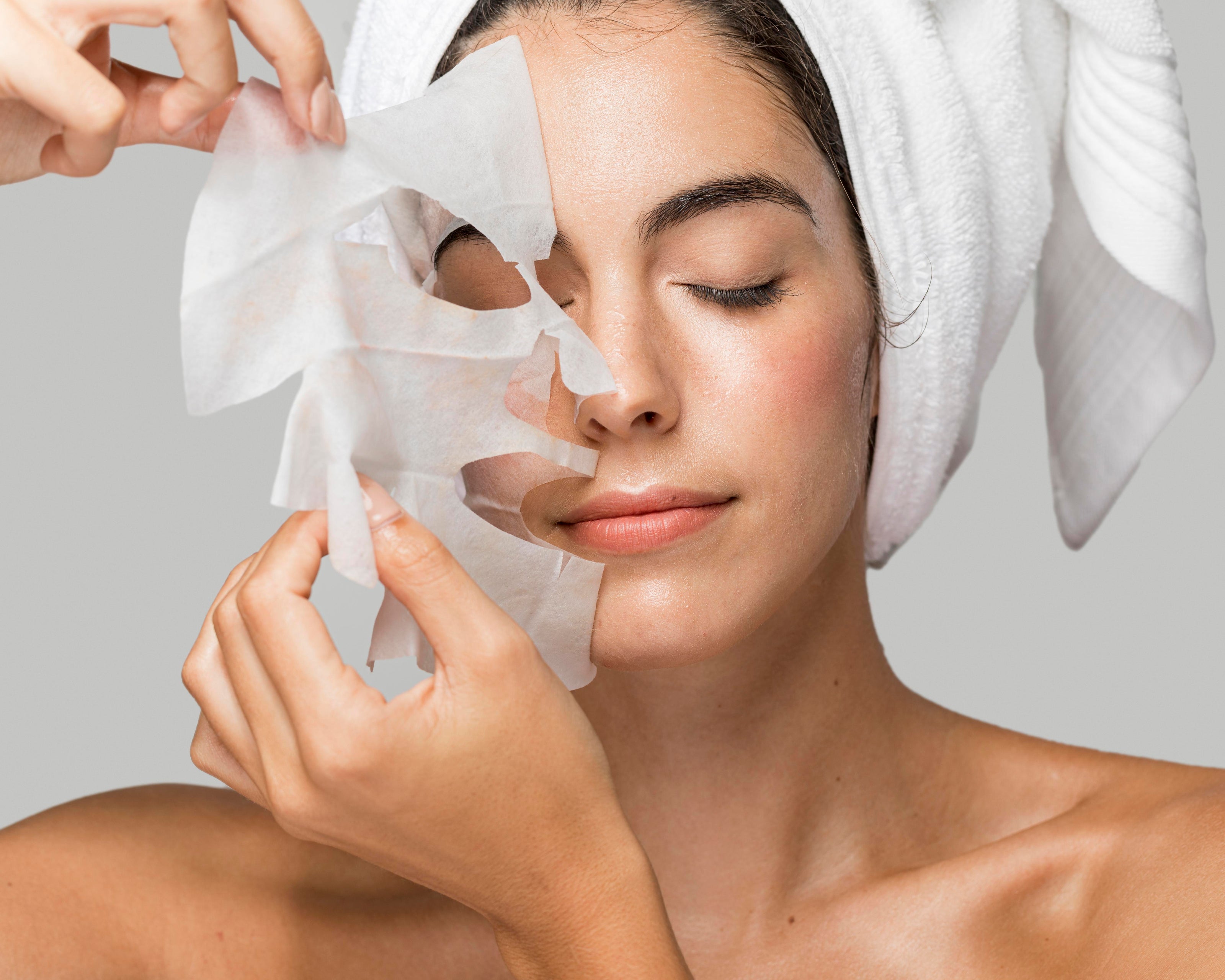 Woman applying O Cosmedics V8 Peptide Complex Mask  with a towel on her head against a neutral background