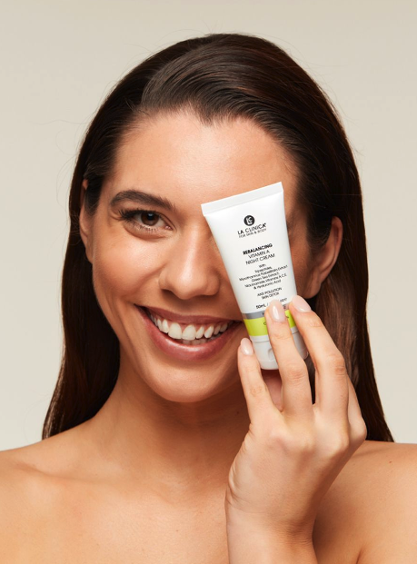 Woman holding a tube of Rebalancing Vitamin A Night Cream against her face.