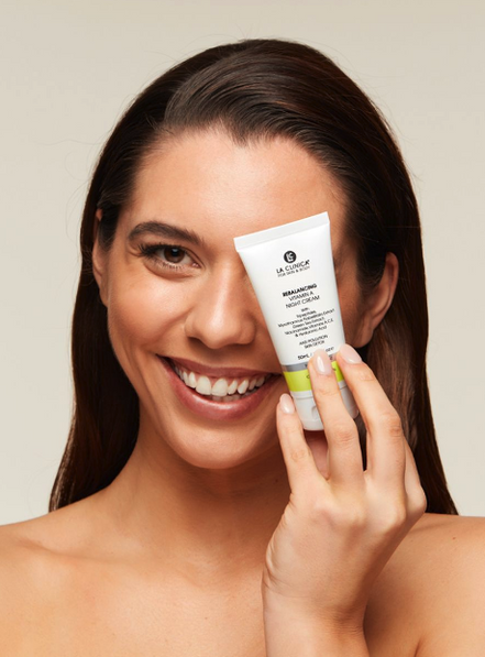 Woman holding a tube of Rebalancing Vitamin A Night Cream against her face.