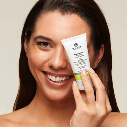 Woman holding a tube of Rebalancing Vitamin A Night Cream against her face.