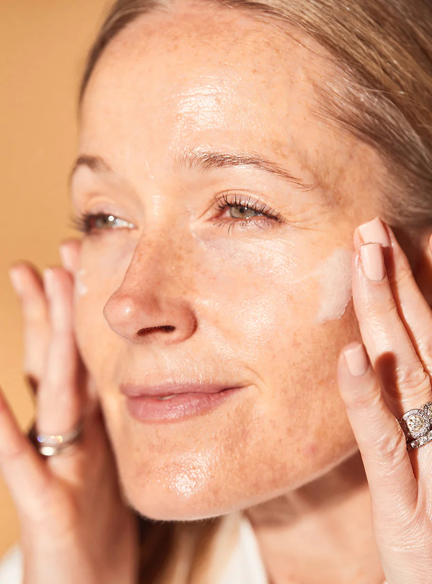 Woman applying Anti Ageing Day Cream With Tripeptides to her face with a neutral background